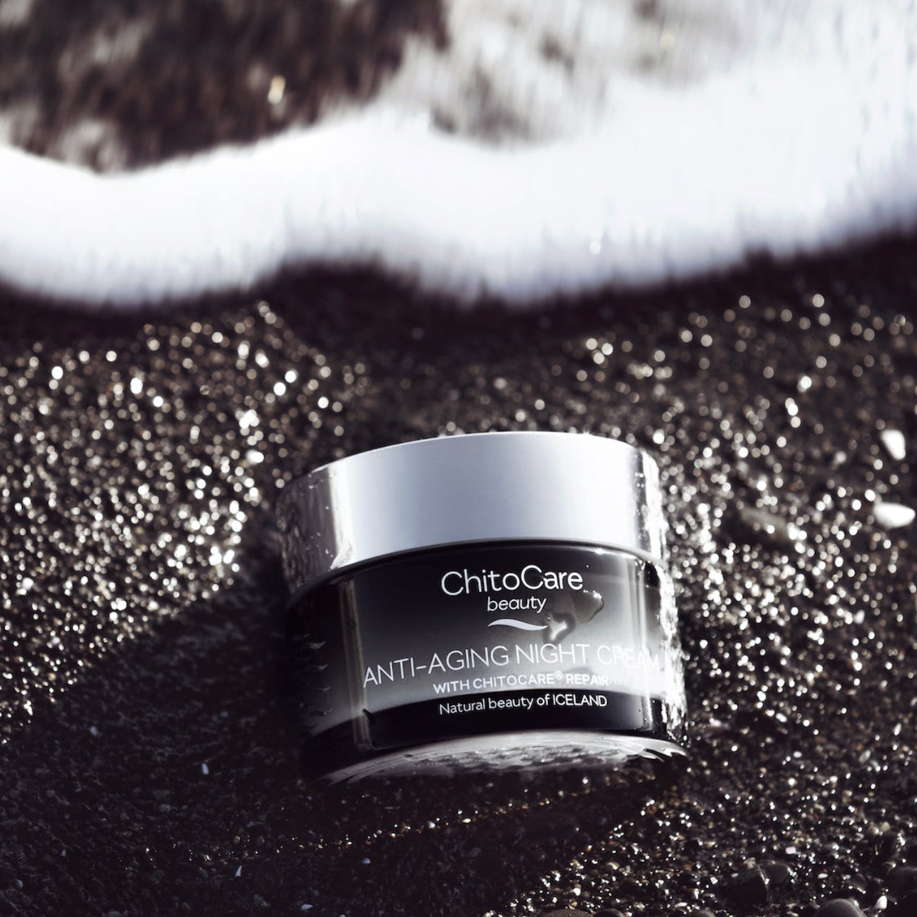 ChitoCare beauty anti-aging night cream jar on a textured black surface with white foam at the top.