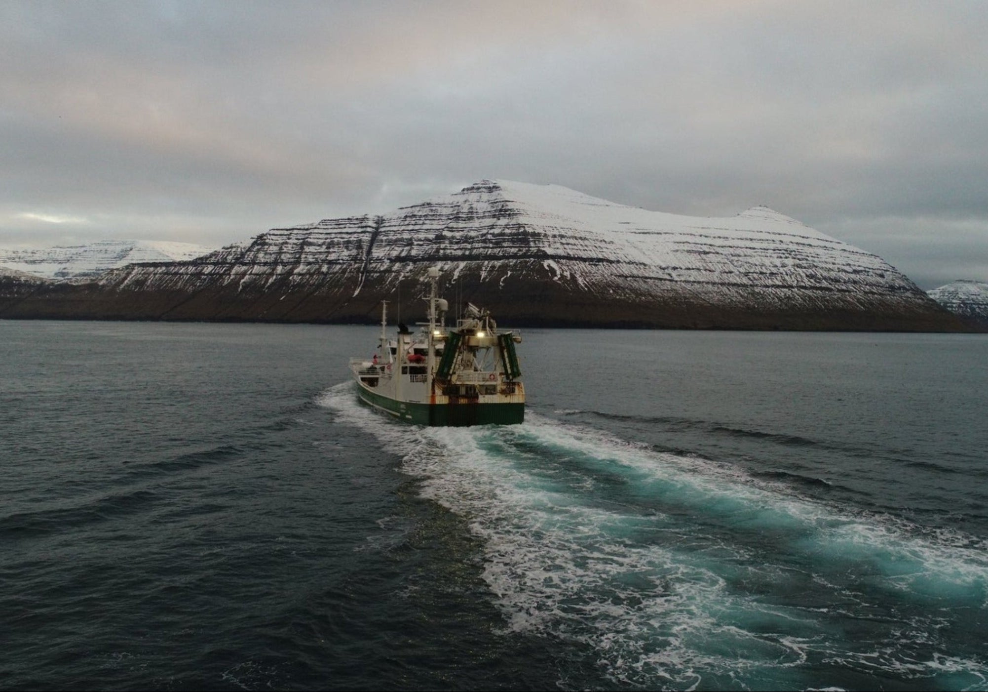 Fishing boat on a body of water with snow-covered mountains in the background