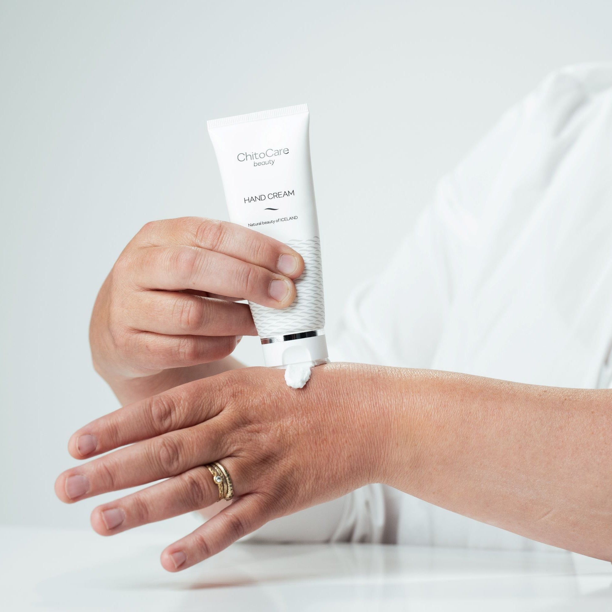 Person applying a white tube of cream to their wrist against a light background
